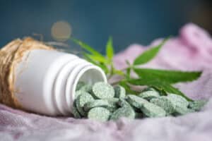 Green medical tablet pills with infused cannabis oil and marijuana leaves closeup