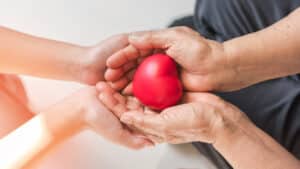 Elderly care with heart in hands of older person, Parkinson disease patient elder senior in support of nursing family caregiver for disability awareness day, National care givers month, hospice palliative care concept