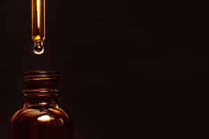 A bottle with a dropper against a black background in warm tones; beauty industry, skincare.